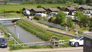 Een stacaravancamping aan de rivier met meerdere stacaravans en een brug over het water.