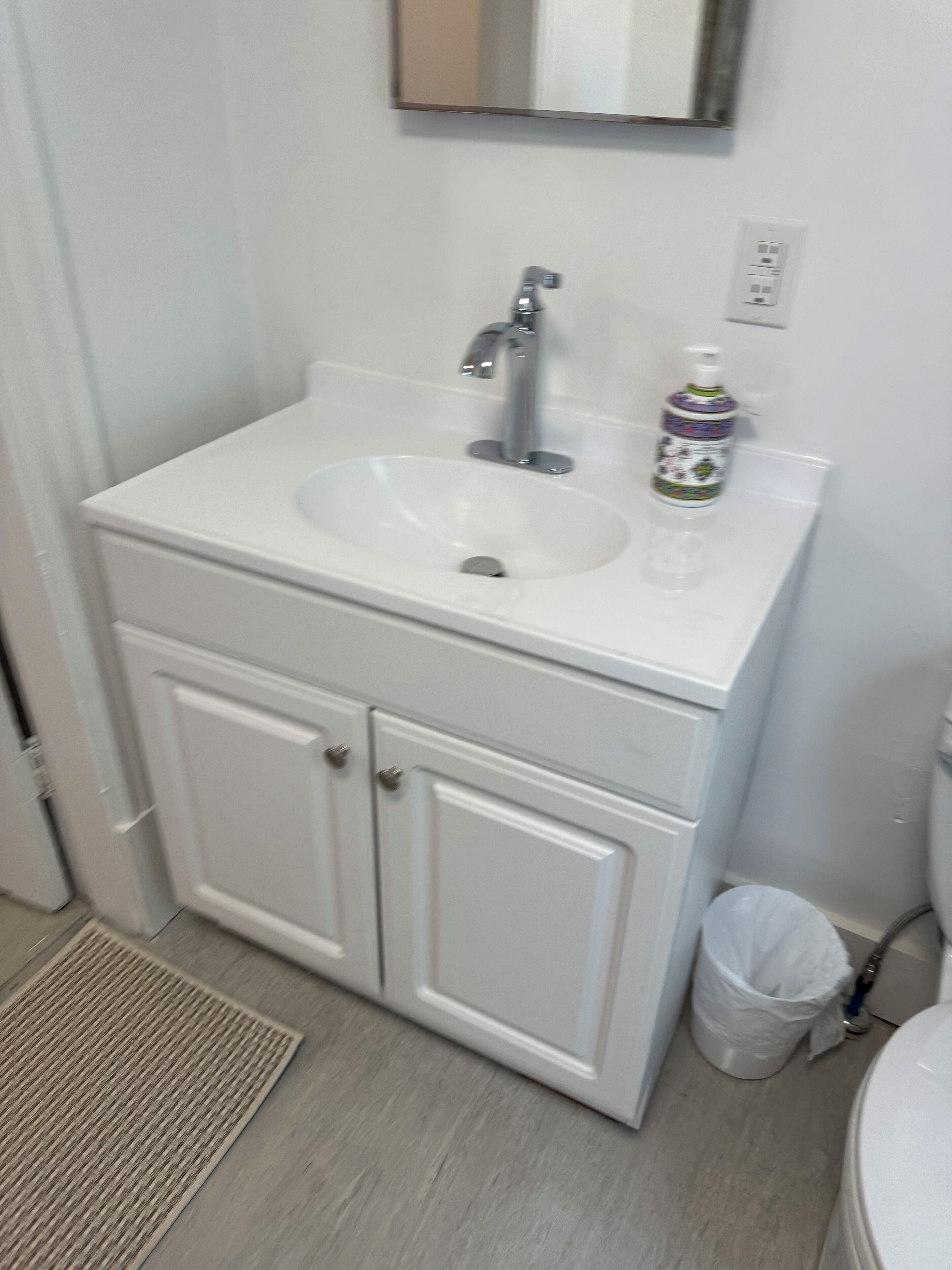 A bathroom with a white sink, a mirror above it, and a trash bin to the right.