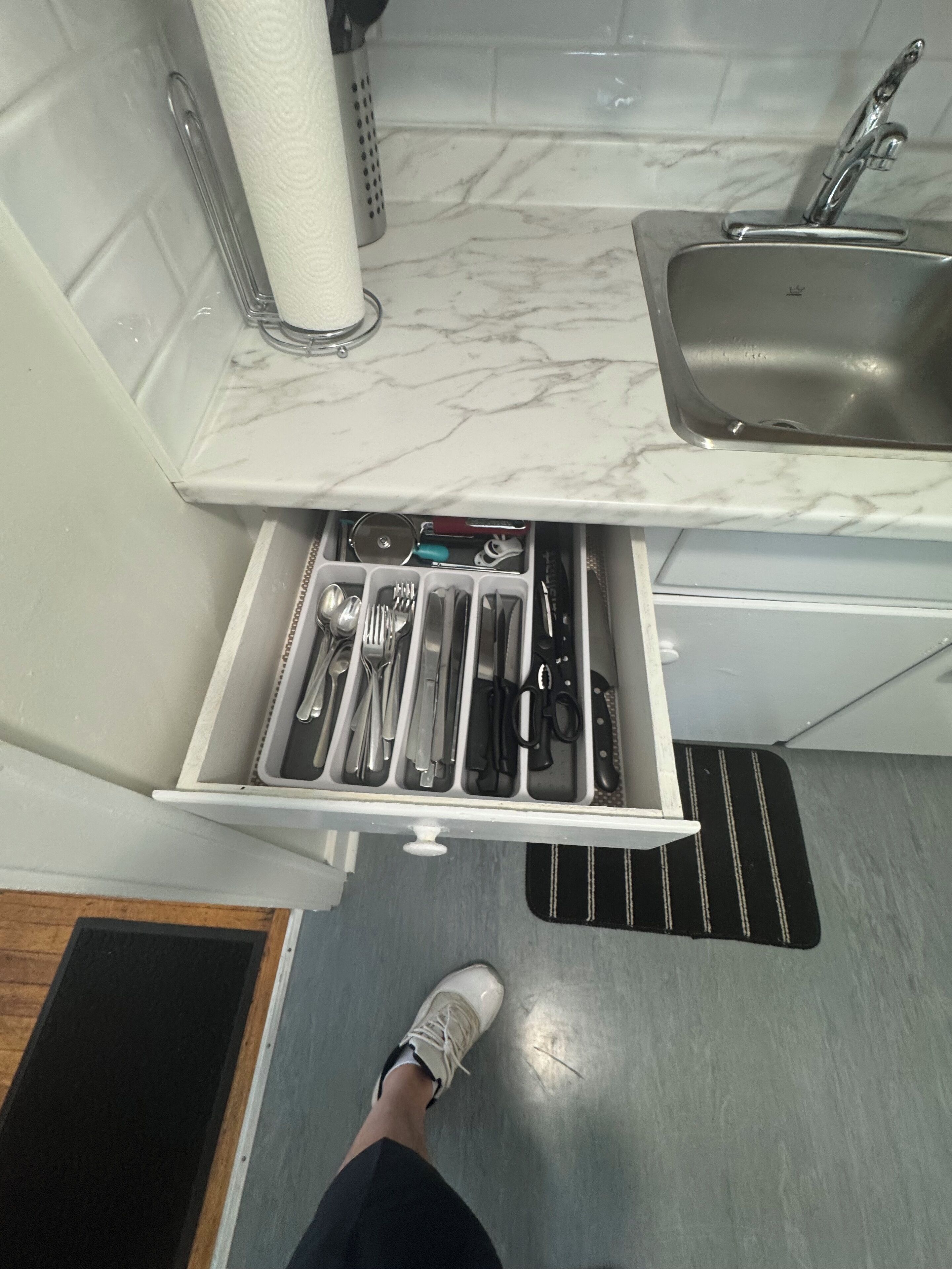 A kitchen with a marble countertop, a stainless steel sink, and a drawer organizer with utensils.