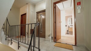Een hotelgang met een trap, een houten deur en een badkamer, zichtbaar door een geopende deur.
