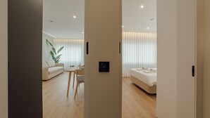 Een moderne hotelkamer met een houten vloer, een bed, een slaapbank en een zithoek met een tafel en stoelen.