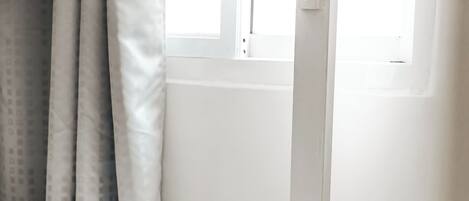 A bed with white bedding and a wooden frame, a window with curtains, and a wooden floor.