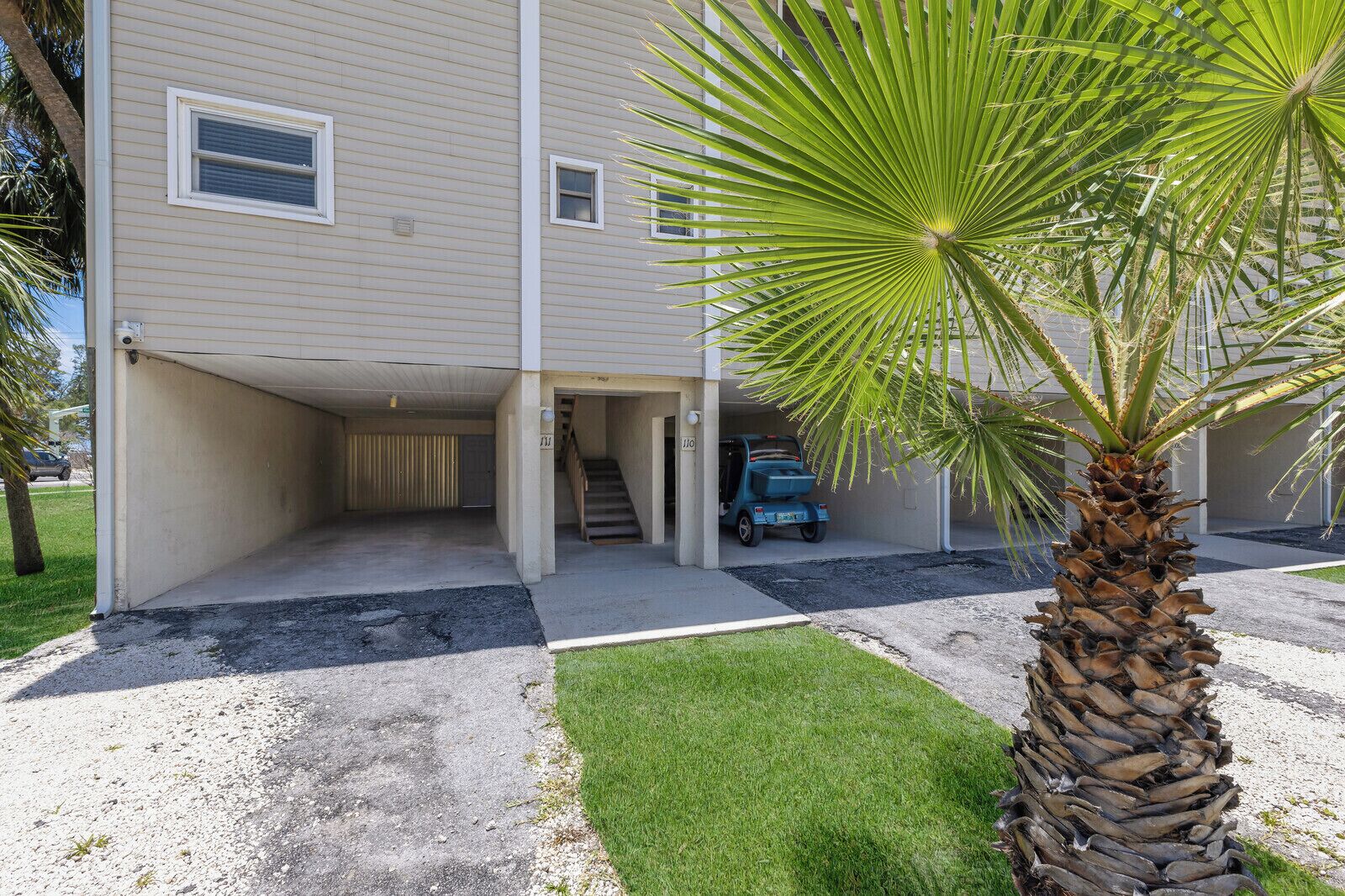 A two-story building with a covered parking area and a palm tree in the foreground.
