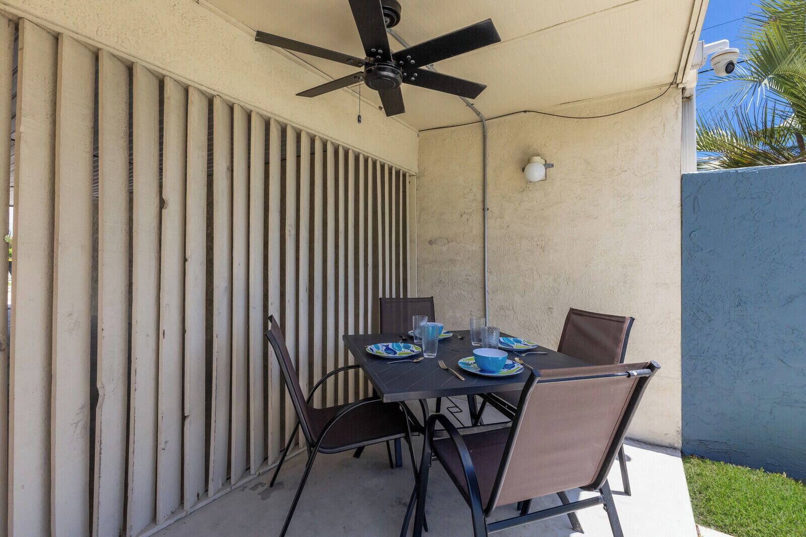Une terrasse extérieure avec une table pour deux, un ventilateur de plafond et une caméra de surveillance.