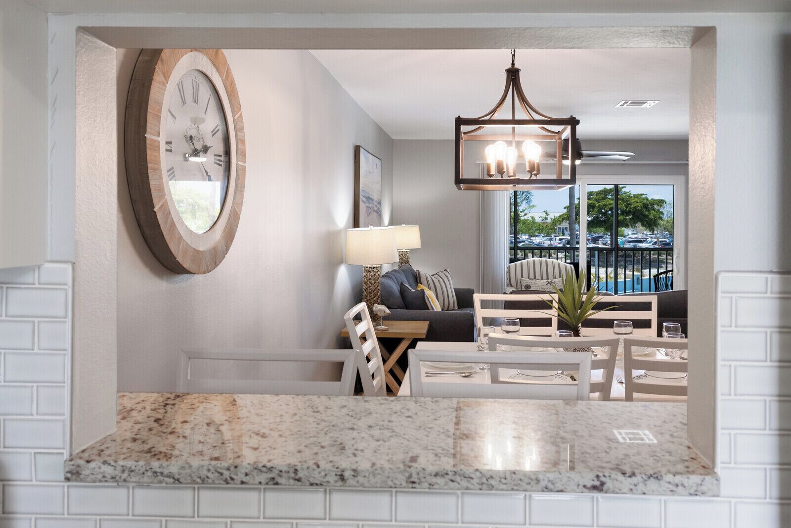 A modern living room with a large clock, a dining area with a marble countertop, and a view of the outdoors through large windows.