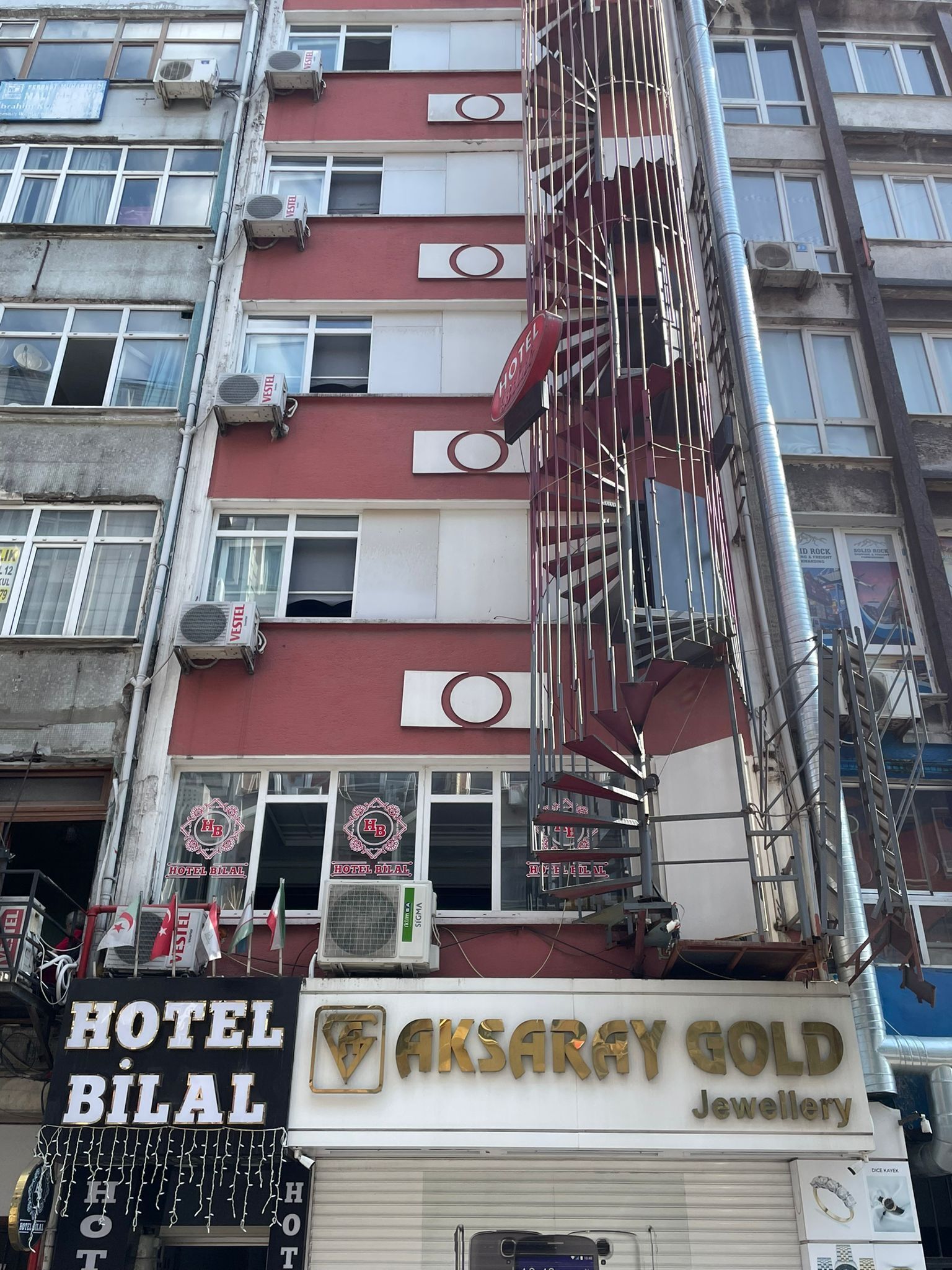 Un immeuble à plusieurs étages, sur lequel on peut voir une enseigne indiquant « Hôtel Bilal » et une bijouterie nommée « Aksaray Gold ».