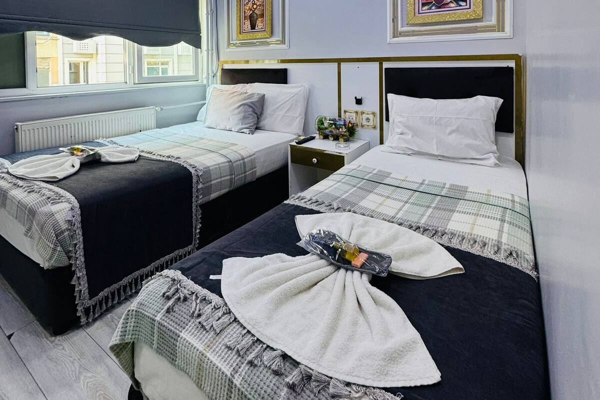 A hotel room with two beds, a window, and a ceiling with blue lighting.