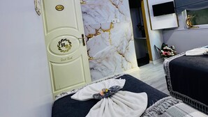 A hotel room with a marble wall, a bed with a checkered blanket, a TV mounted on the wall, and a door with a number plate. - BİLAL HOTEL (Istanbul)