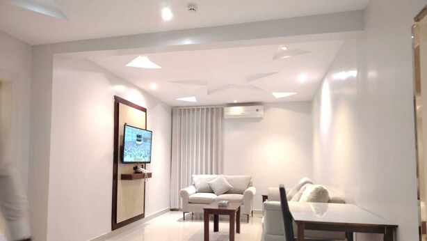 A modern hotel room with a flat-screen TV, a sofa, a dining table, and a chair. - Rama Dubai Hotel Suites 1 (Riyadh)