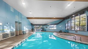 Una piscina interior con agua azul cristalina, terraza de madera y ventanas amplias.