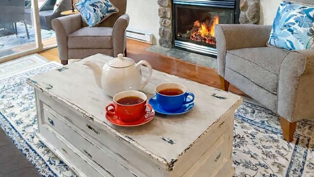 Un salón acogedor con chimenea, un televisor montado encima y una mesa de centro con tazas y una tetera.