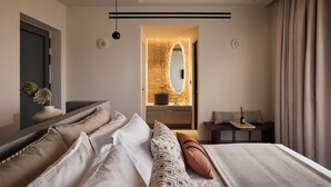 A modern bedroom with a large bed, a vanity with a mirror, and a small table with a lamp. - Kemelia Suites (Milos)