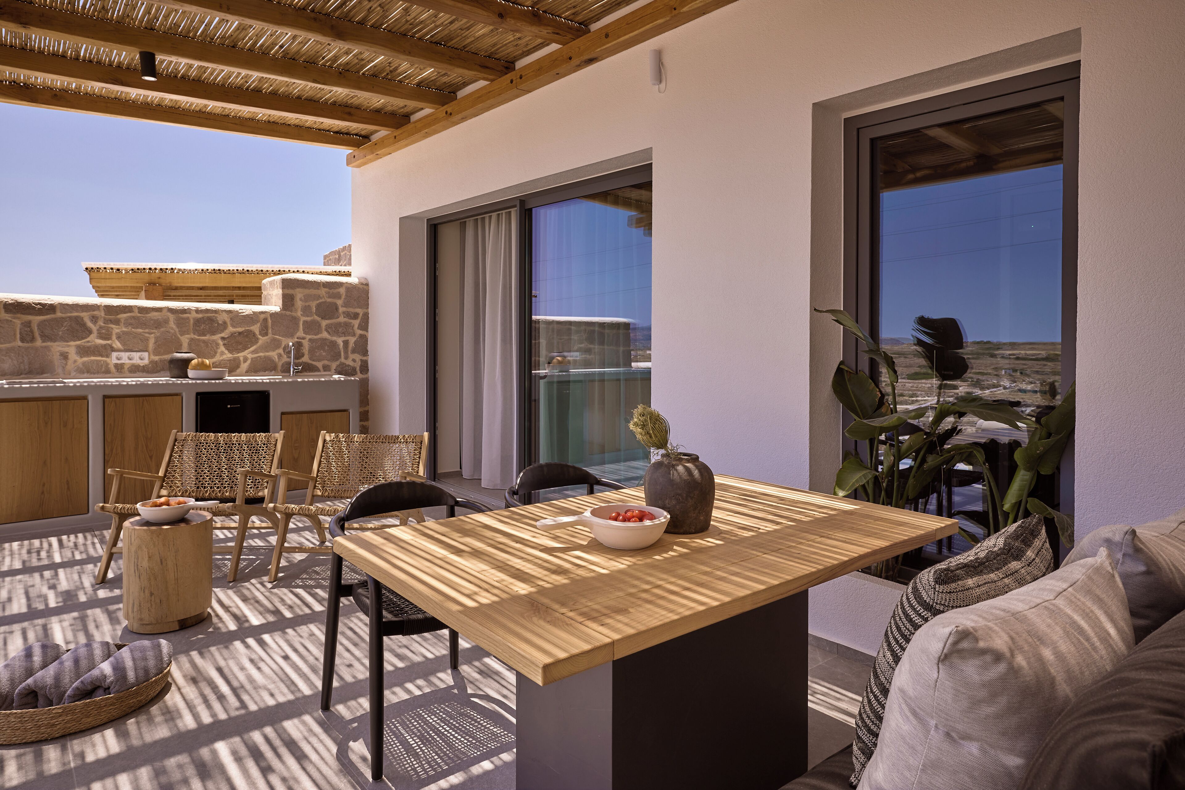 A modern outdoor dining area with a wooden table, wicker chairs, and a stone wall backdrop.