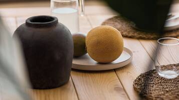 Une table en bois, sur laquelle se trouvent un vase en céramique, une carafe en verre, un verre et un set de table en fibres tressées.