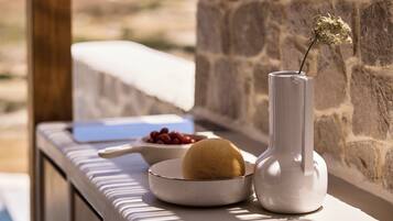 A stone wall, a white vase with a dried flower, a bowl of red berries, and a melon on a table.