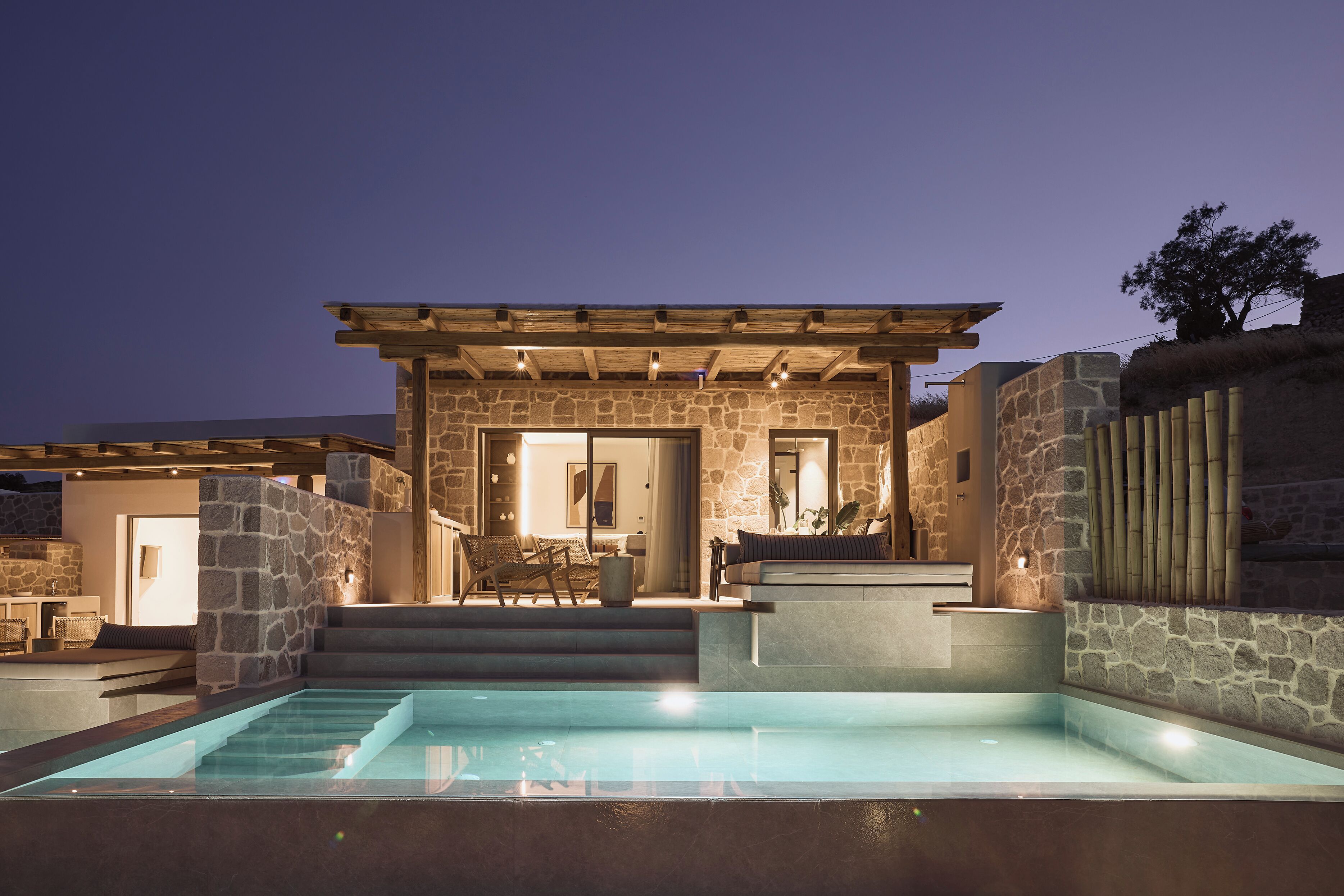 A stone building with a pool, steps leading to a covered patio, and outdoor seating.