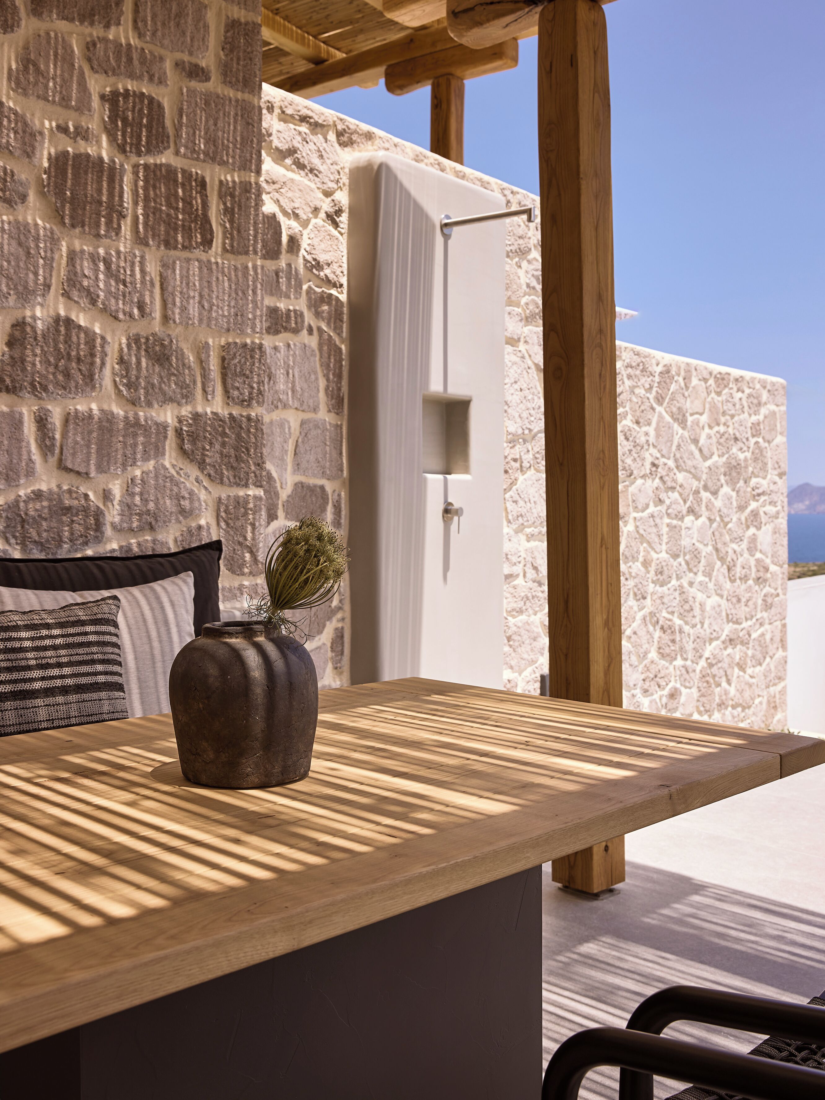 Un muro de piedra con una mesa de madera y un florero.