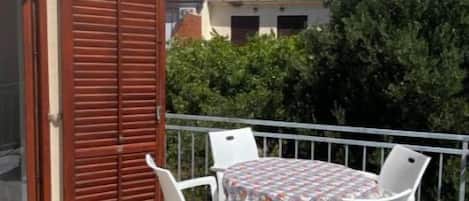 A balcony with a table and chairs, a wooden shutter door, and a mountain view in the background.