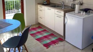 Una cocina compacta con armarios blancos, un refrigerador pequeño y una zona de comedor con mesa y sillas.
