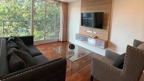 Ein modernes Wohnzimmer mit großem Fenster, Flachbildfernseher, Glastisch und einer Couch.