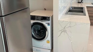 Eine kompakte Küche mit Edelstahlkühlschrank, Waschmaschine und Marmorarbeitsplatte.