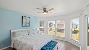 A bedroom with a bed, a ceiling fan, a bench, and large windows.