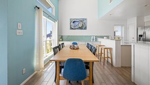 A modern kitchen with a dining area, featuring a large wooden table, blue chairs, and a kitchen island with a refrigerator and sink.