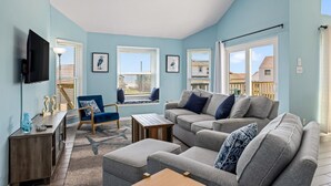 A living room with a sofa set, a wooden coffee table, a blue armchair, and a TV mounted on the wall.