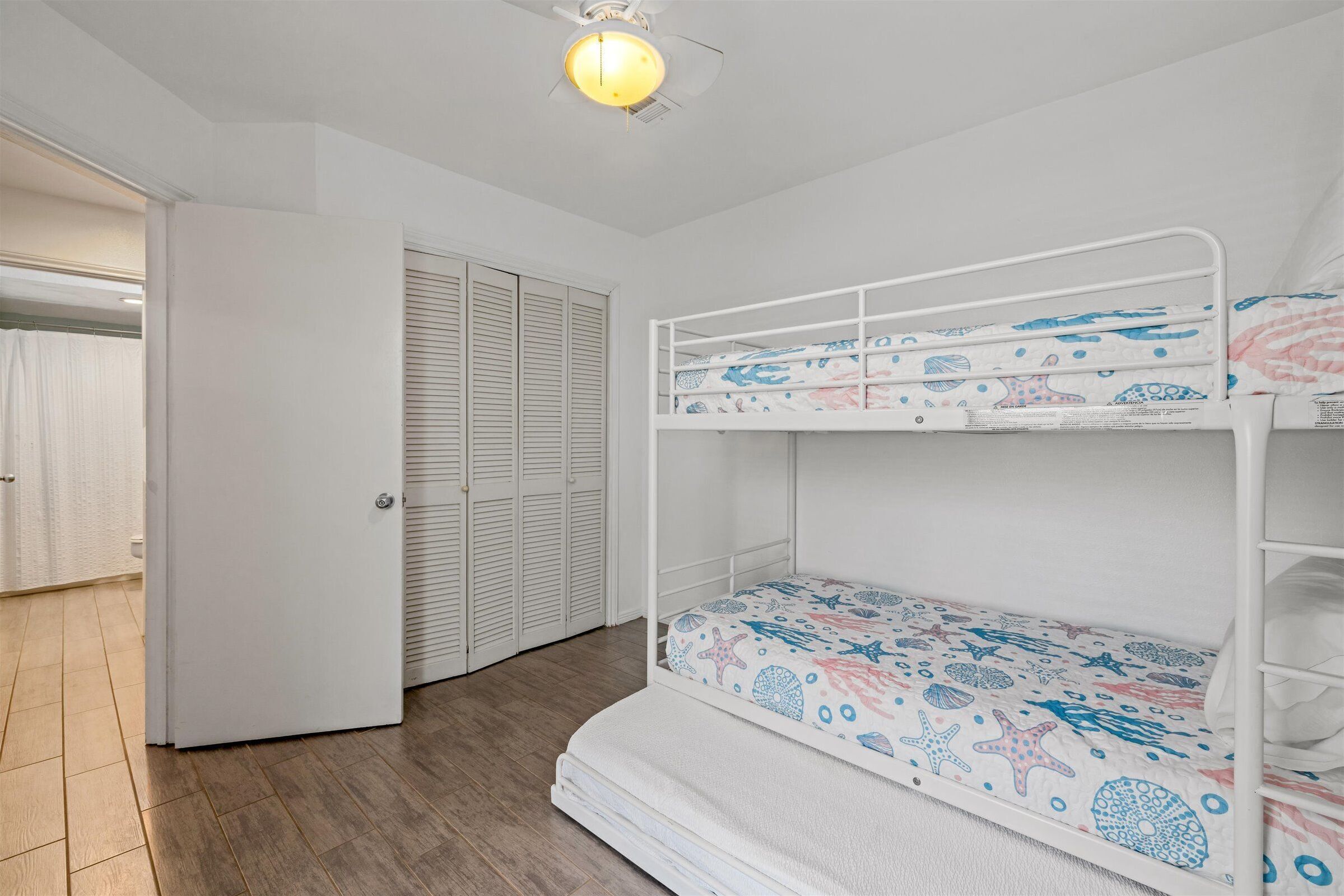 A bunk bed with a patterned bedspread, a white ceiling fan, and a closed door in the background.