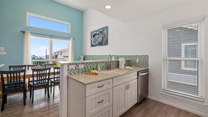 A kitchen with a dining area, featuring a kitchen island, white cabinets, a tiled backsplash, and a window with blinds.