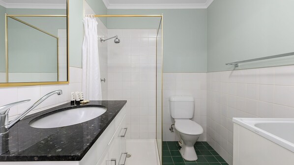 A bathroom with a white sink, toilet, and bathtub, a shower with a gold frame, and a mirror with a gold frame.
