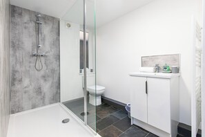 A modern bathroom with a glass-enclosed shower, a white toilet, and a white sink with a mirror above it. - Victoria Apartments (Hartlepool)