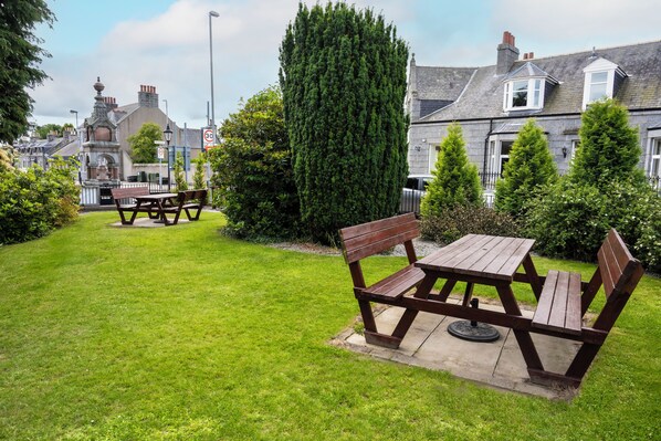 A well-maintained garden with a picnic table and benches, surrounded by neatly trimmed hedges and a tall coniferous tree. - Haughton Arms Hotel (Alford)
