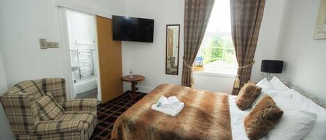 A hotel room with a bed, a sofa, a TV, and a window with curtains.