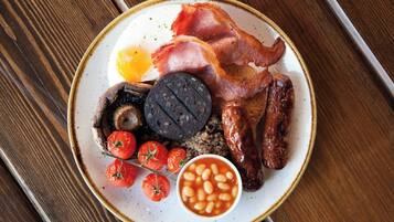 Un plato de comida para el desayuno con tocino, salchichas, huevos, tomates y frijoles.