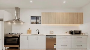 A modern kitchen with white cabinetry, stainless steel appliances, and a wooden accent wall. - Black Shack - 13 Paisley Island (Paisley)