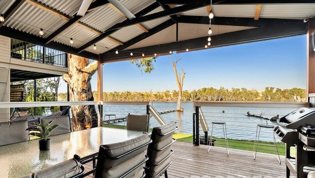 An outdoor deck with a glass table and chairs, overlooking a lake with a barbecue grill and a view of the surrounding trees. - Black Shack - 13 Paisley Island (Paisley)
