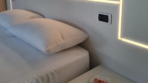 A modern hotel room with a neatly made bed, a bedside table with a plate of food, and a wall-mounted control panel.