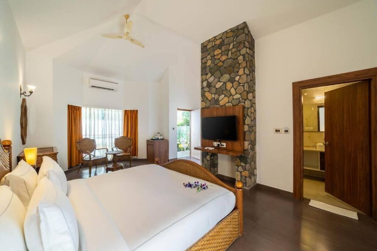 A spacious bedroom with a large bed, a stone accent wall, a flat-screen TV, and a ceiling fan.