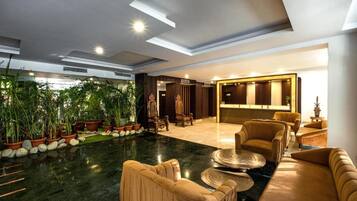 A spacious lobby with a marble floor, plush seating, and a variety of plants.