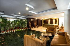 A spacious lobby with a marble floor, plush seating, and a variety of plants.