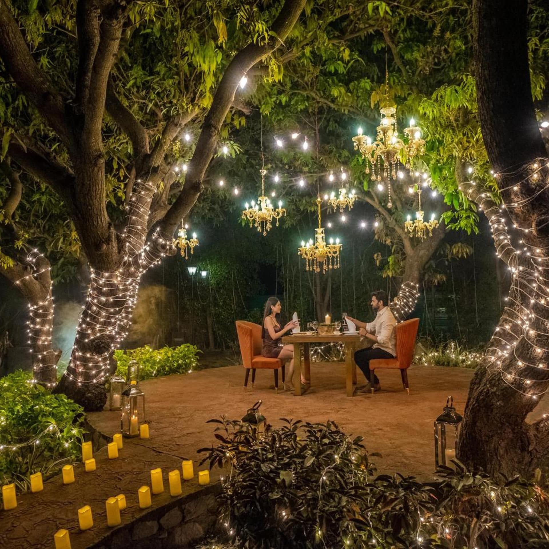 An outdoor dining area with a table and chairs, surrounded by trees and string lights.