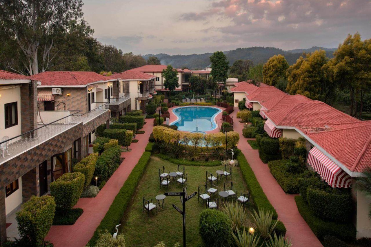 A hotel courtyard with a swimming pool, multiple dining areas, and a red-roofed building.