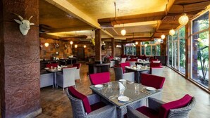 A restaurant with wicker furniture, red cushions, and a rustic interior. - Country Inn Tarika Riverside Resort Jim Corbett (Ramnagar)