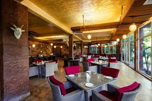 A restaurant with wicker furniture, red cushions, and a rustic interior.