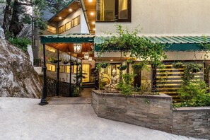 A multi-level building with a covered entrance, stone walls, and hanging plants. - Country Inn Tarika Riverside Resort Jim Corbett (Ramnagar)