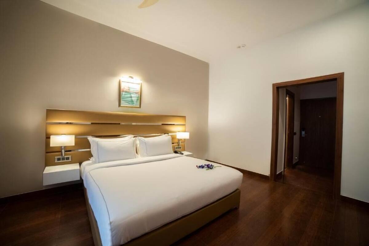 A hotel room with a large bed, bedside lamps, a nightstand, and a door to another room.