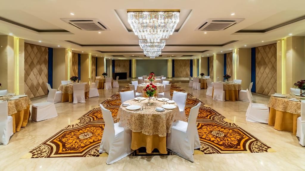 A banquet hall with round tables, white chairs, and a large chandelier.