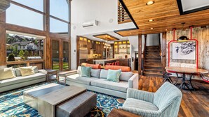 A spacious living area with a large sofa, coffee table, and a patterned rug. A staircase leads to an upper level with a kitchen and dining area.