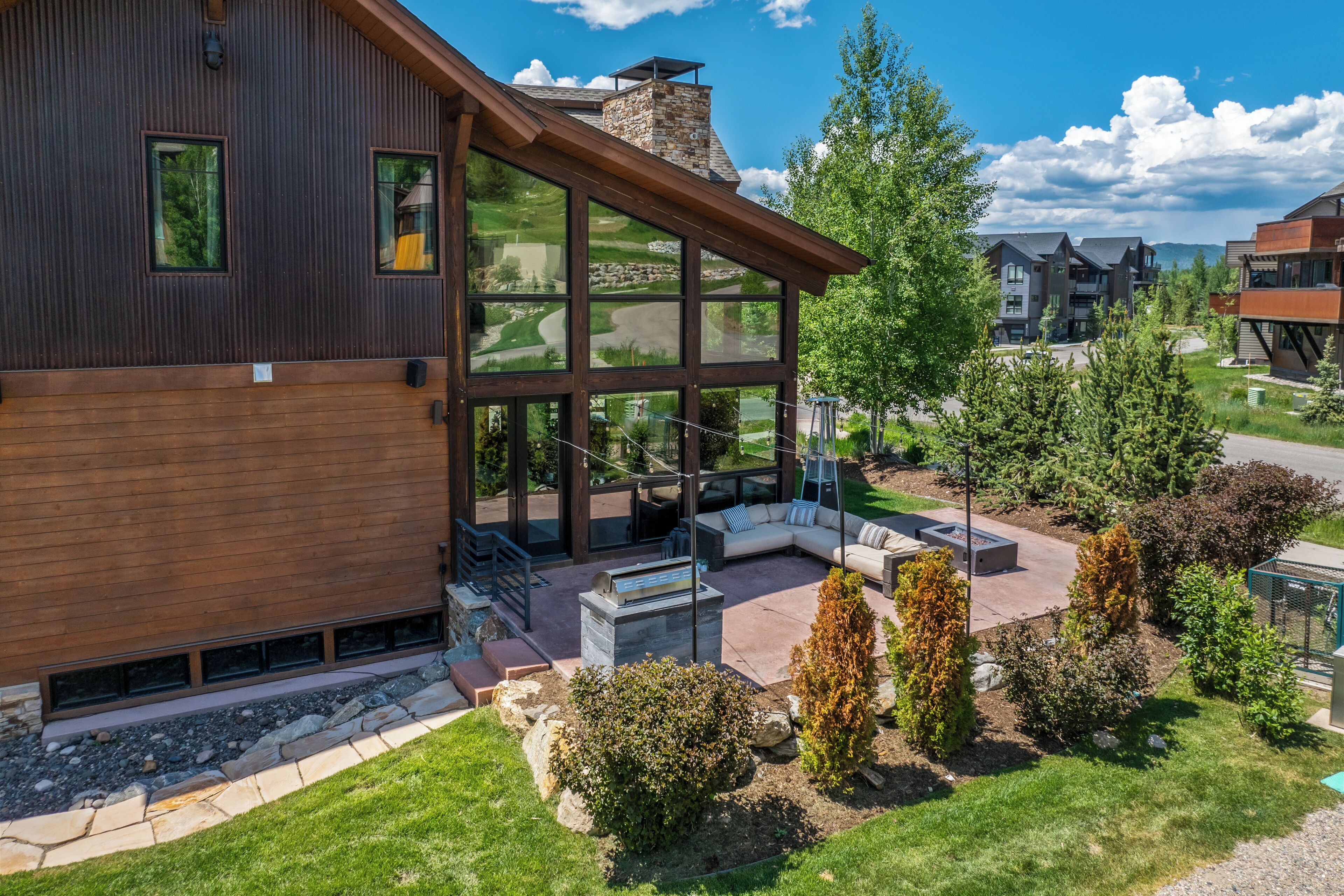 A modern house with a large glass window, a stone chimney, and a well-maintained garden.